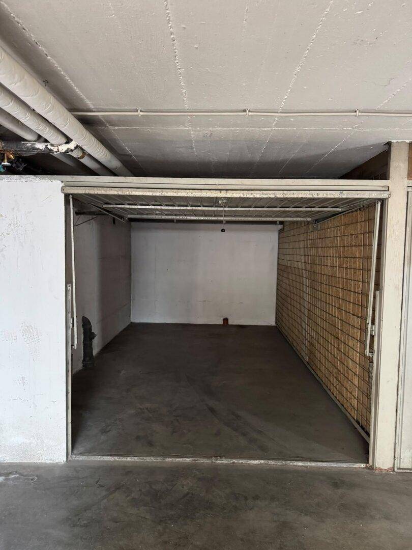 Leerer Lagerraum mit Betonboden und Gitterwand in einem Garagenkomplex, ideal für zusätzlichen Stauraum.