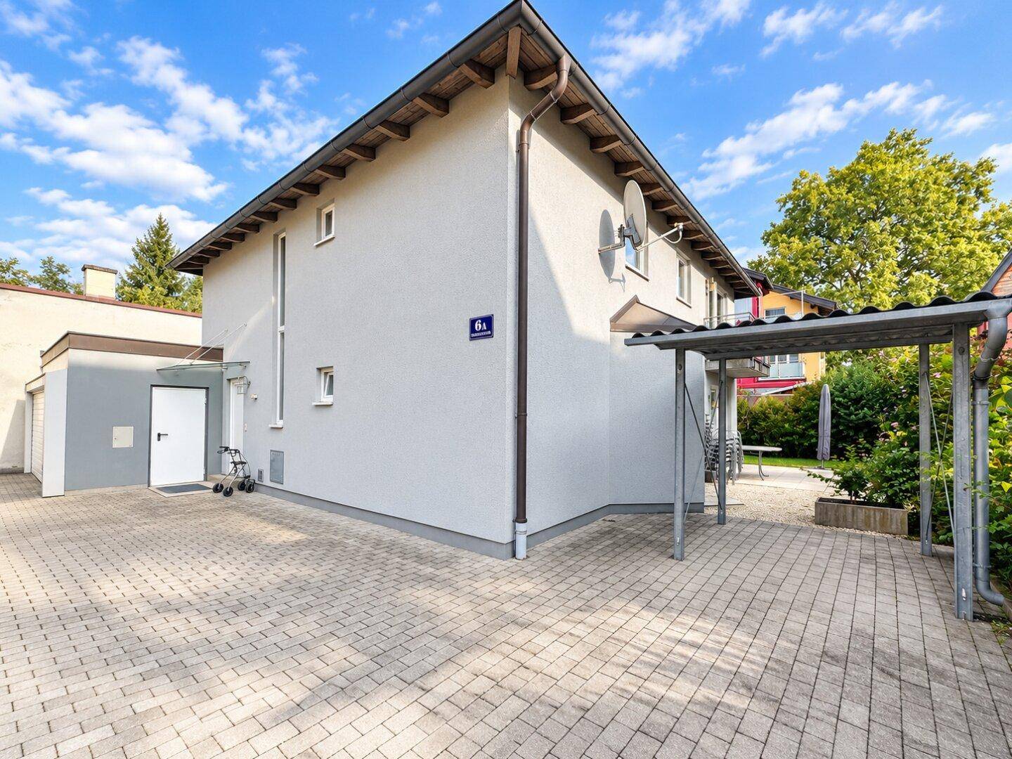 Modernes Mehrfamilienhaus mit gepflastertem Vorplatz und überdachtem Carport.