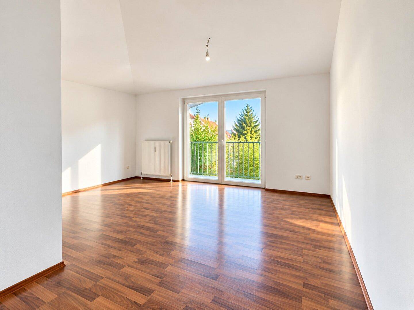 Helles Zimmer mit Laminatboden und großem Fenster mit Blick ins Grüne.