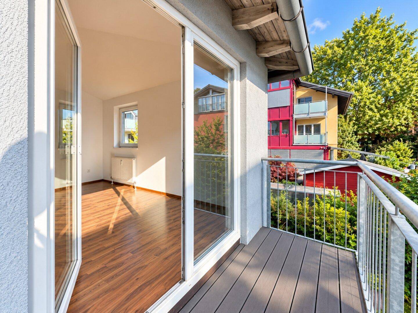 Balkon mit Holzdielen und Metallgeländer, der einen Blick in einen hellen Innenraum bietet.