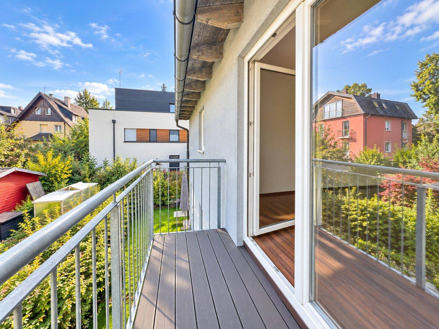 Geräumiger Balkon mit Holzdielen und Blick auf die umliegenden Häuser und viel Grün.