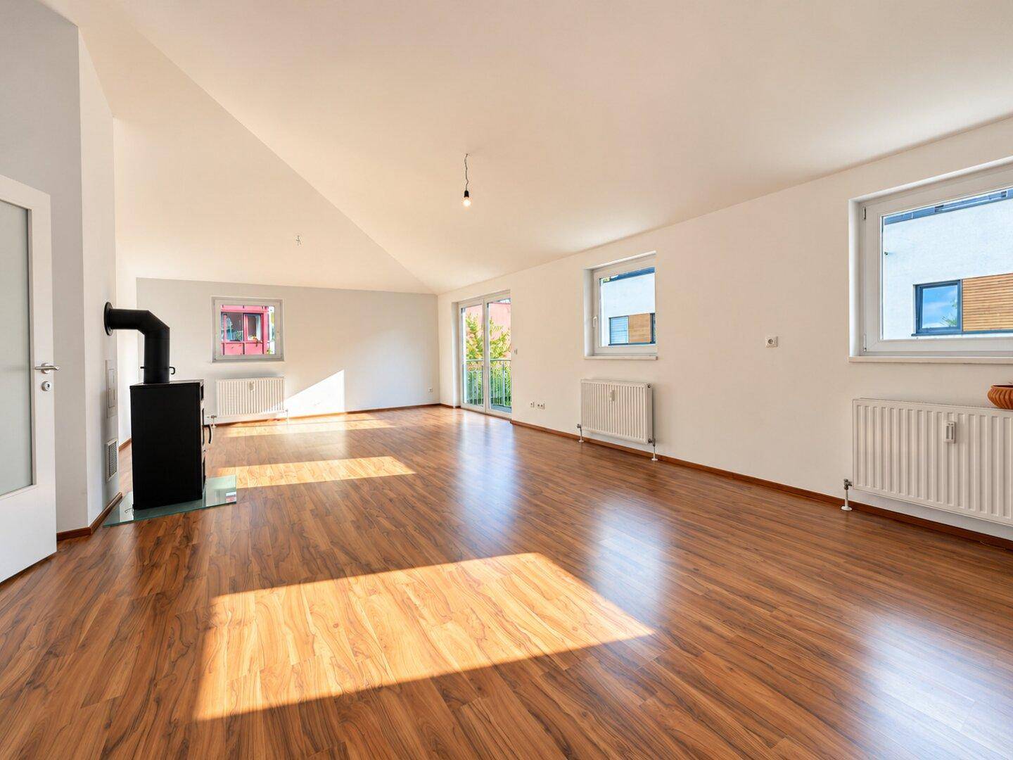Geräumiges, lichtdurchflutetes Wohnzimmer mit Laminatboden und mehreren Fenstern.