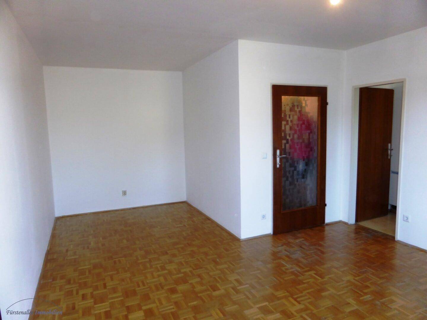 Leerer Raum mit Parkettboden, weißen Wänden und zwei Türen, eine davon mit Glaseinsatz.