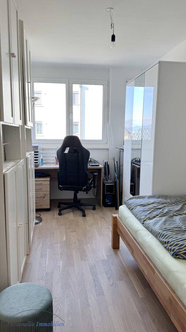 Helles Schlafzimmer mit Schreibtisch, Einbauschränken und Blick auf die Umgebung.