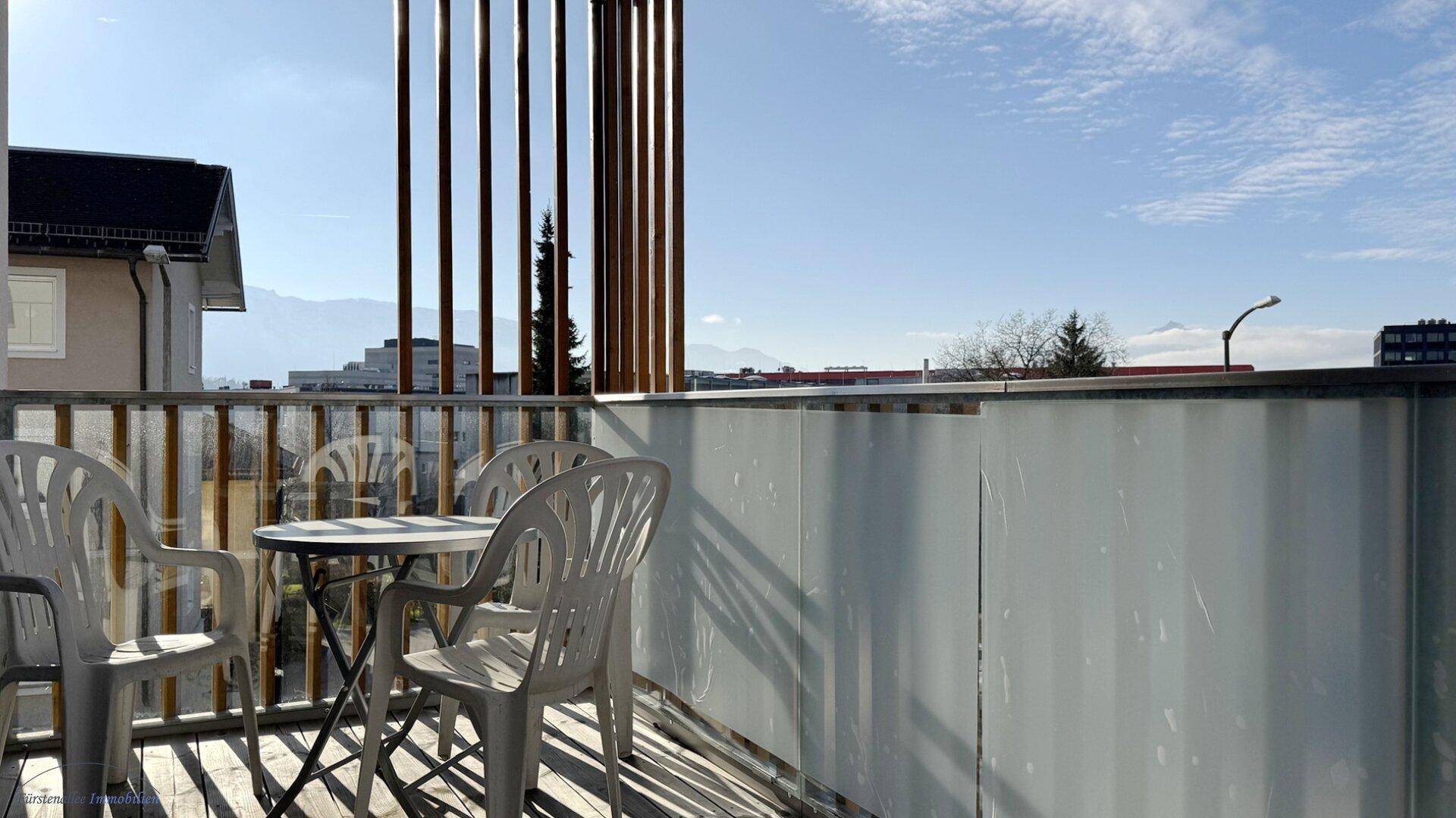 Sonniger Balkon mit Gartenmöbeln und weitem Blick auf die umliegende Landschaft und Berge.