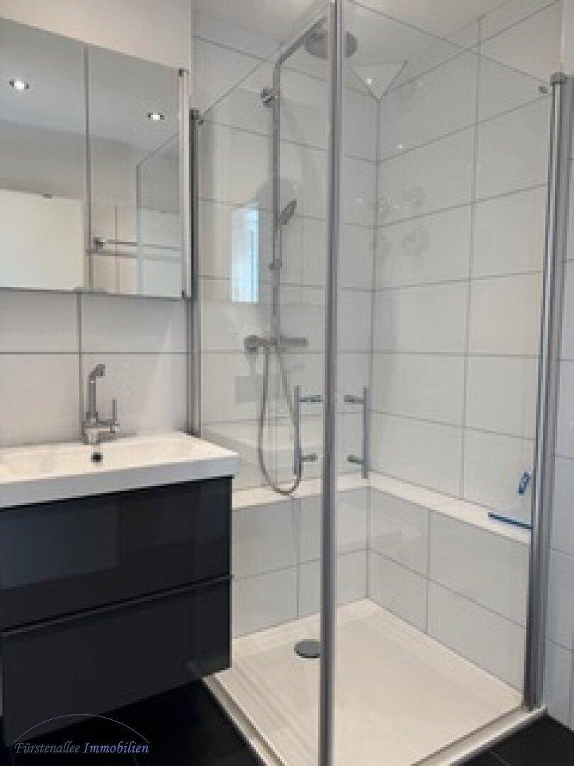 Modernes Badezimmer mit weiß gefliesten Wänden, Duschkabine und Waschtisch mit Unterschrank.