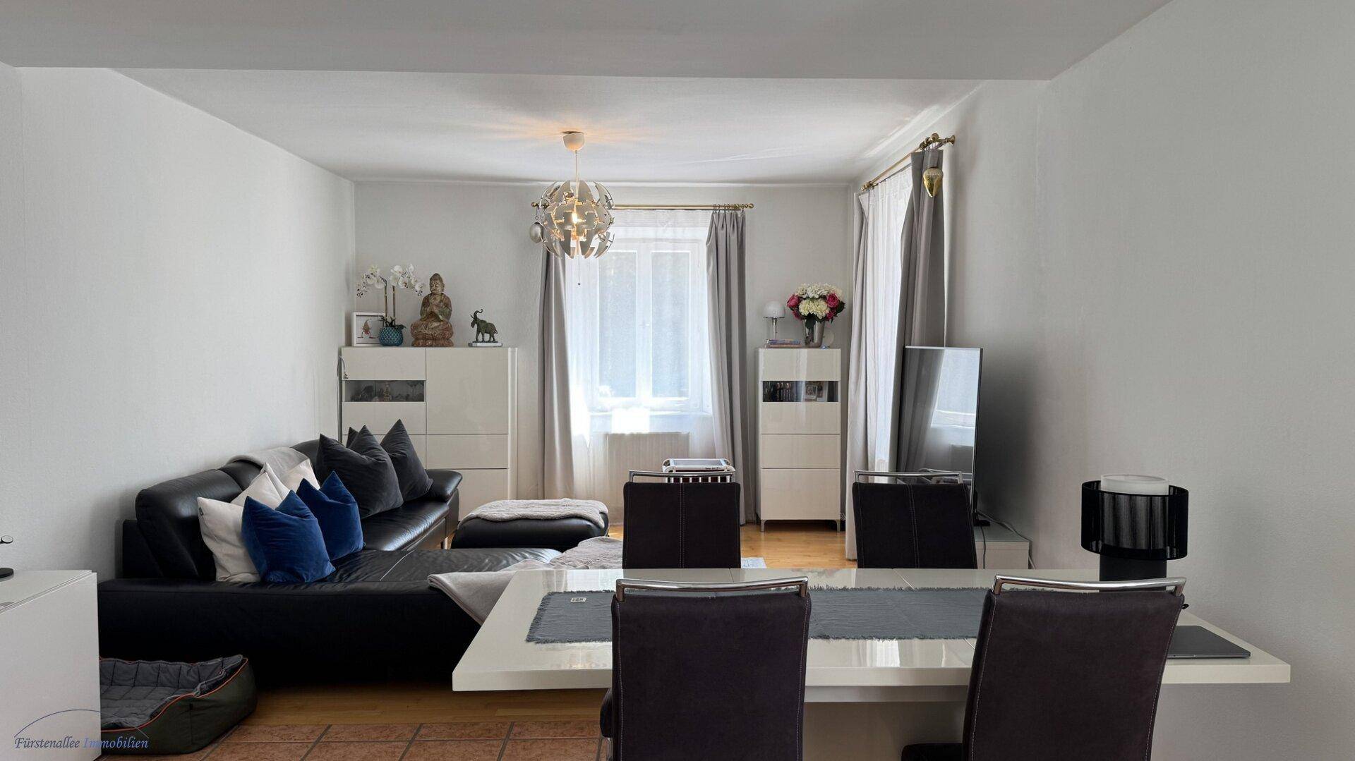 Heller offener Wohn- und Essbereich mit modernem Sofa, Esstisch und Fliesenboden.