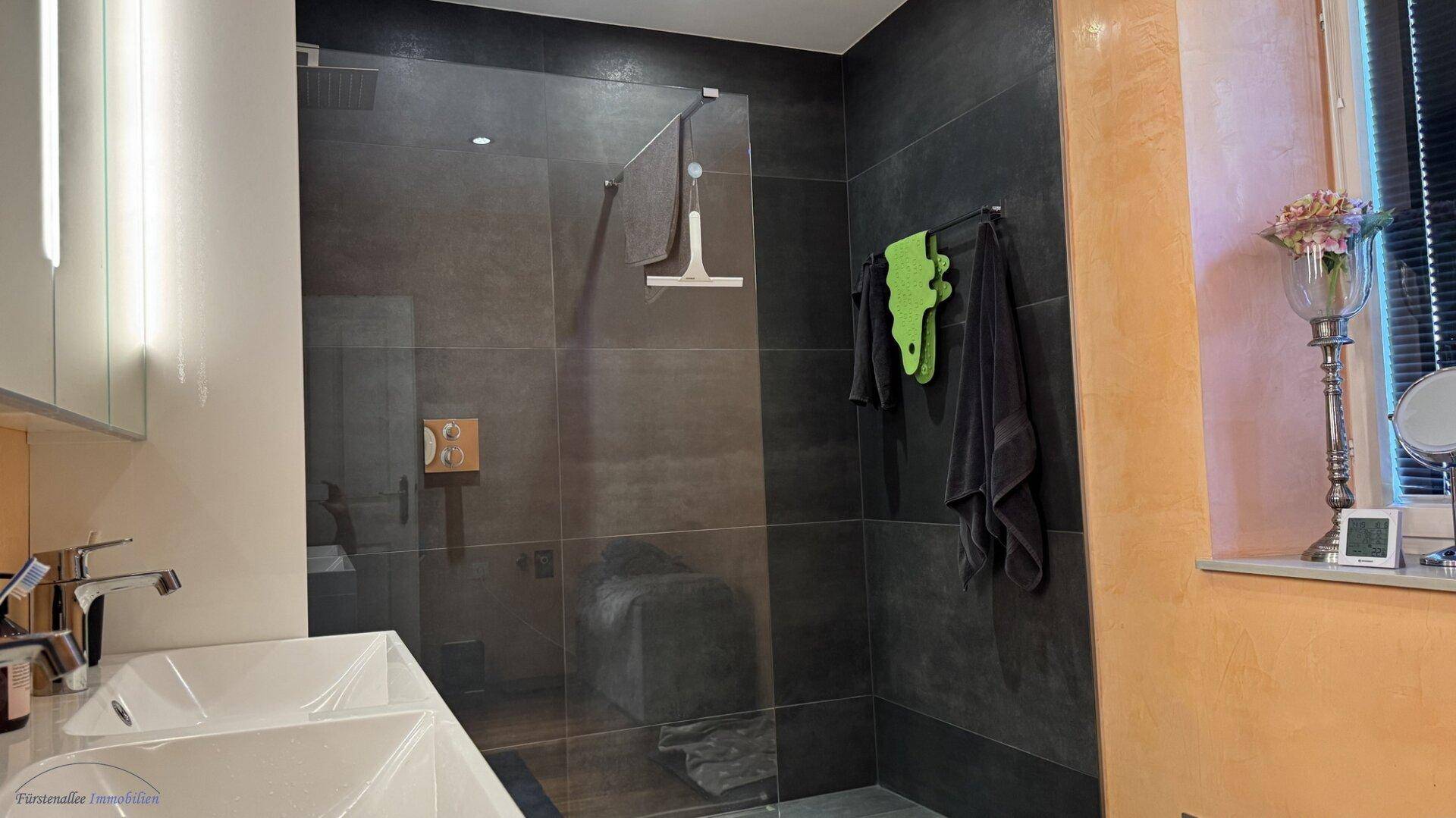 Elegantes Badezimmer mit großer begehbarer Dusche, Doppelwaschbecken und dunklen Fliesen.