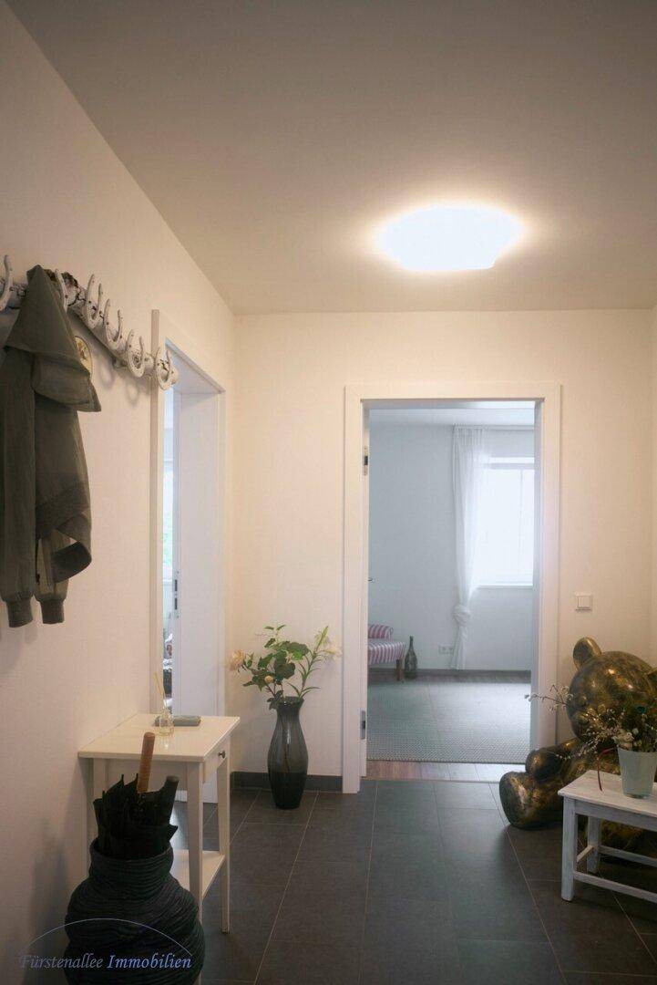 Heller Flur mit dunklen Fliesen, Garderobe und offenen Türen zu angrenzenden Räumen.