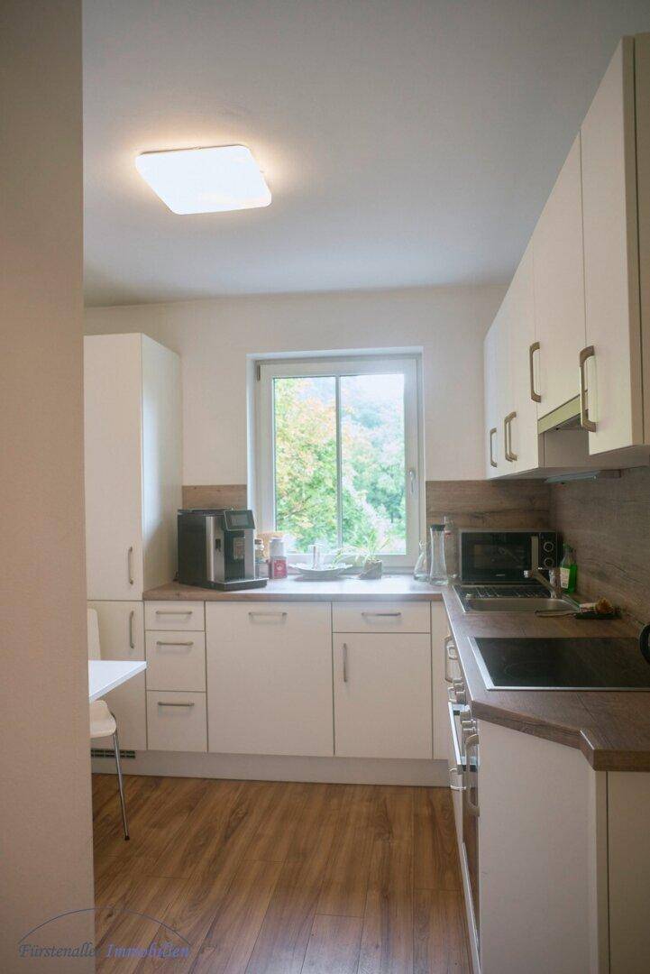 Moderne Einbauküche in Weiß mit Laminatboden, Fenster und Blick ins Grüne, ausgestattet mit Geräten.