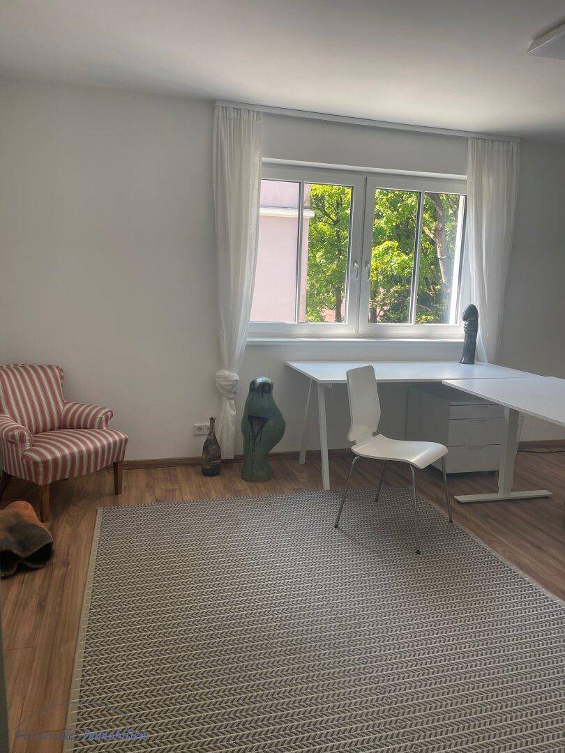 Geräumiges Arbeitszimmer mit einem bequemen Sessel, zwei Schreibtischen und einem Fenster mit Ausblick.