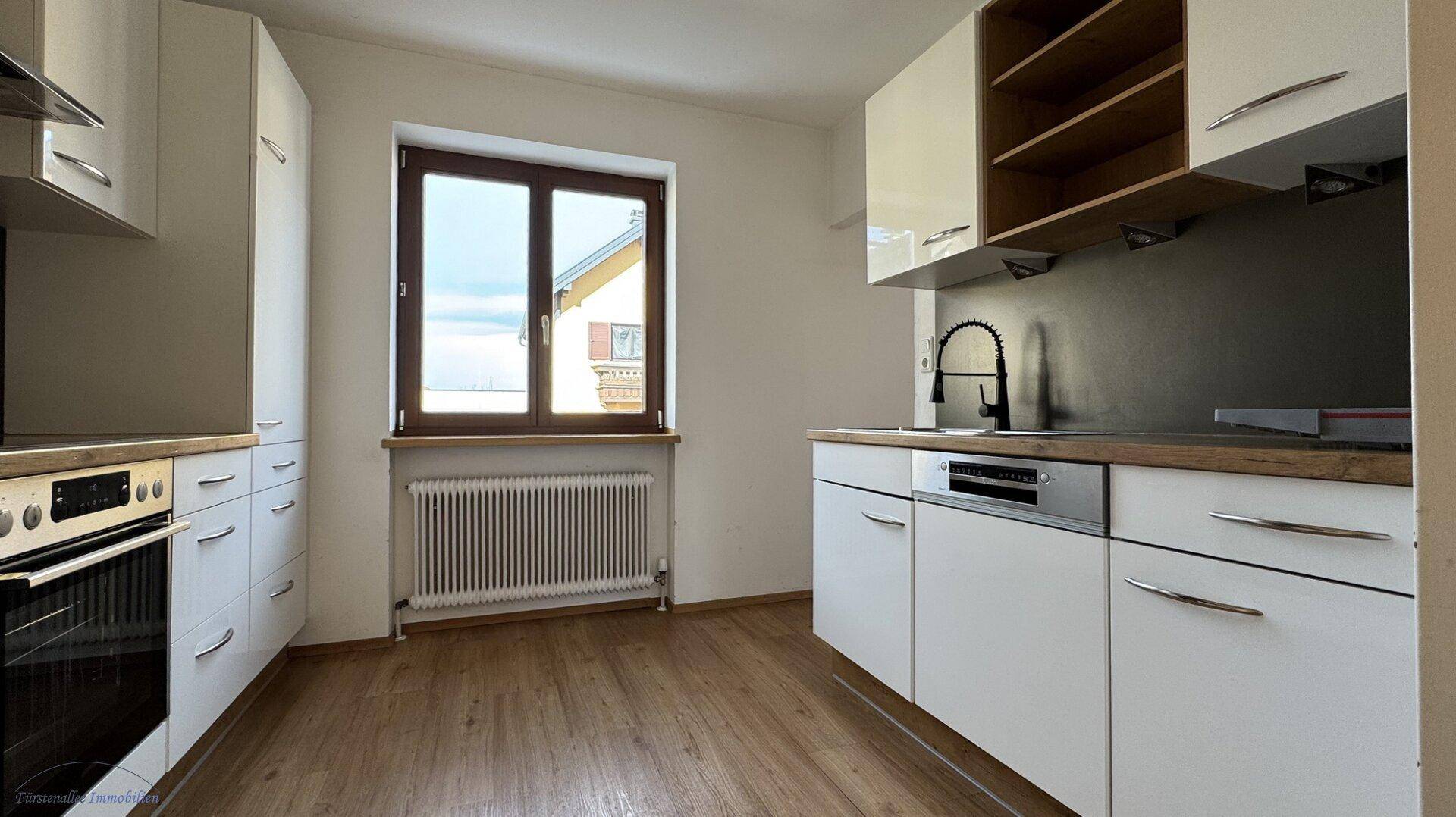 Funktionale Küche mit weißen Schränken, Holzarbeitsplatte und Fenster mit Blick nach draußen.