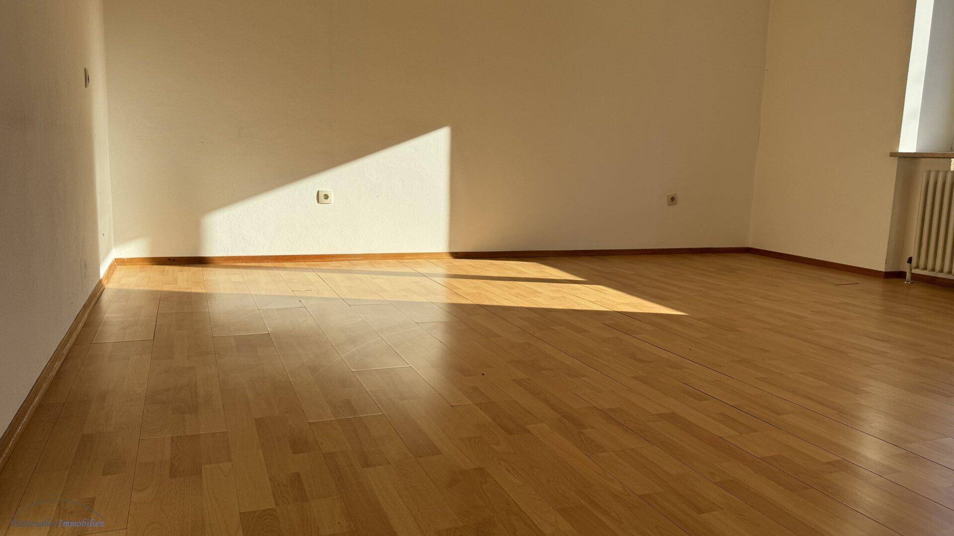 Geräumiger, heller Raum mit Holzboden, der von der Nachmittagssonne durchflutet wird.