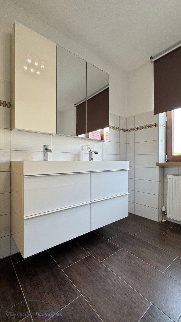 Modernes Badezimmer mit Doppelwaschbecken, Spiegelschrank und dunklen Fliesen.