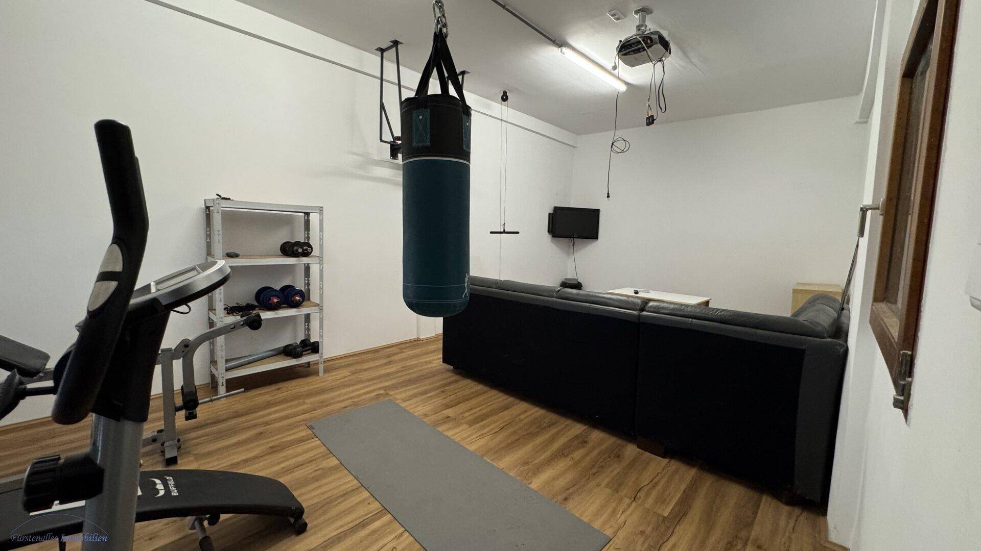 Vielseitiger Raum mit Fitnessgeräten, Boxsack und Projektor, ideal als Heim-Fitnessstudio oder Medienraum.