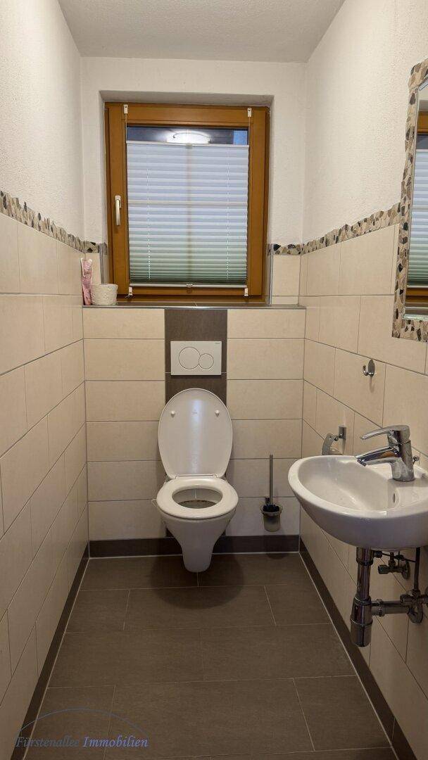 Kleines Gäste-WC mit Fenster, Wand-WC und Waschbecken, hell gefliest.