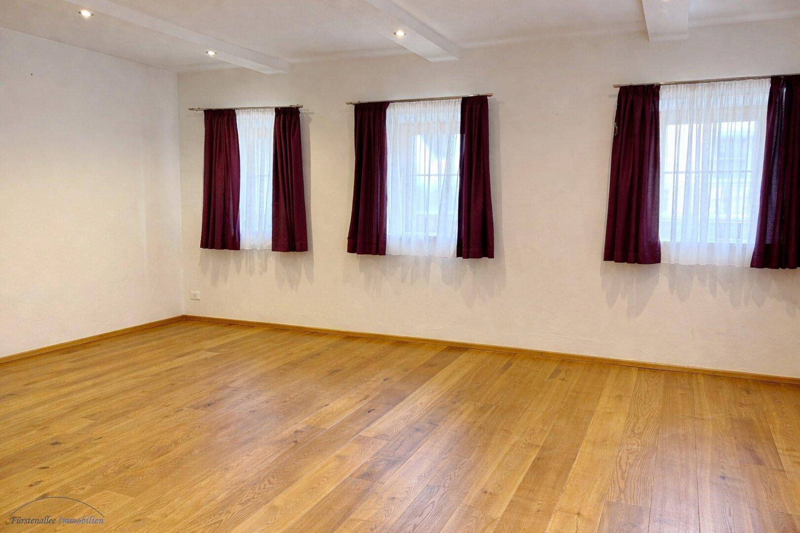 Heller, leerer Raum mit Holzboden und drei Fenstern, bereit zur individuellen Gestaltung.