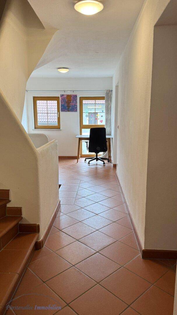 Heller Flur mit Terrakotta-Fliesenboden und Blick auf einen Arbeitsbereich mit Fenster.