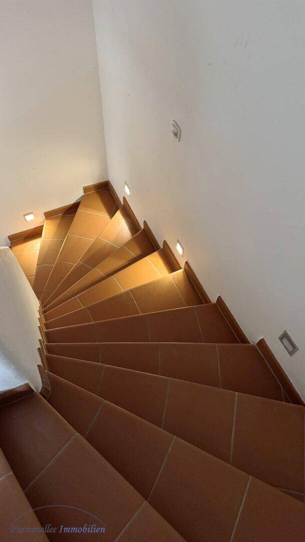 Geschwungene Treppe mit Terrakotta-Stufen und integrierter Beleuchtung, die in die obere Etage führt.
