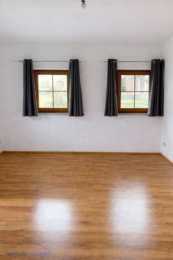 Freundlicher Raum mit Holzboden und zwei Fenstern, ideal als Schlaf- oder Arbeitszimmer.
