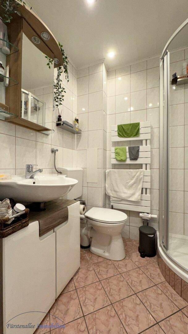 Badezimmer mit Dusche, WC, Einzelwaschbecken und beheiztem Handtuchhalter.