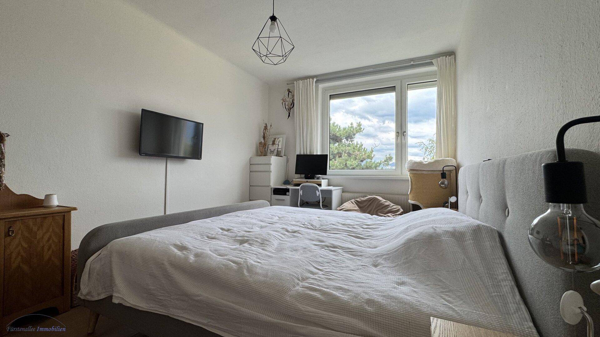 Schlafzimmer mit großem Bett, Fernseher und Fenster mit Blick ins Grüne.