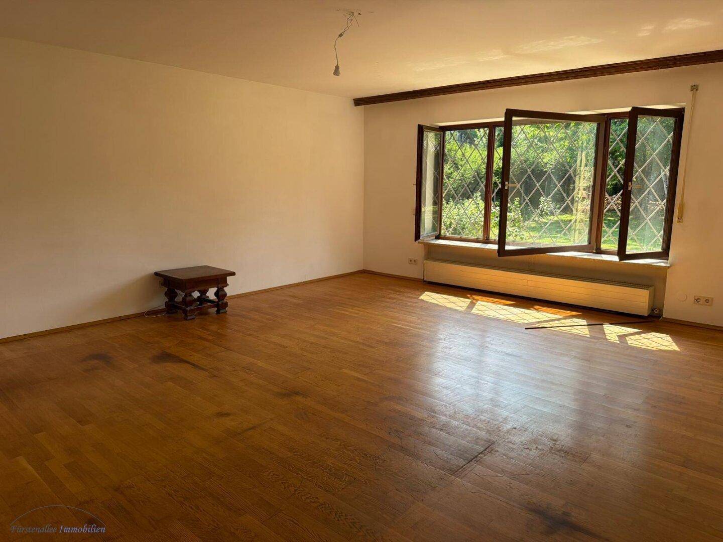 Helles Wohnzimmer mit Holzboden, großen Fenstern und Blick ins Grüne.