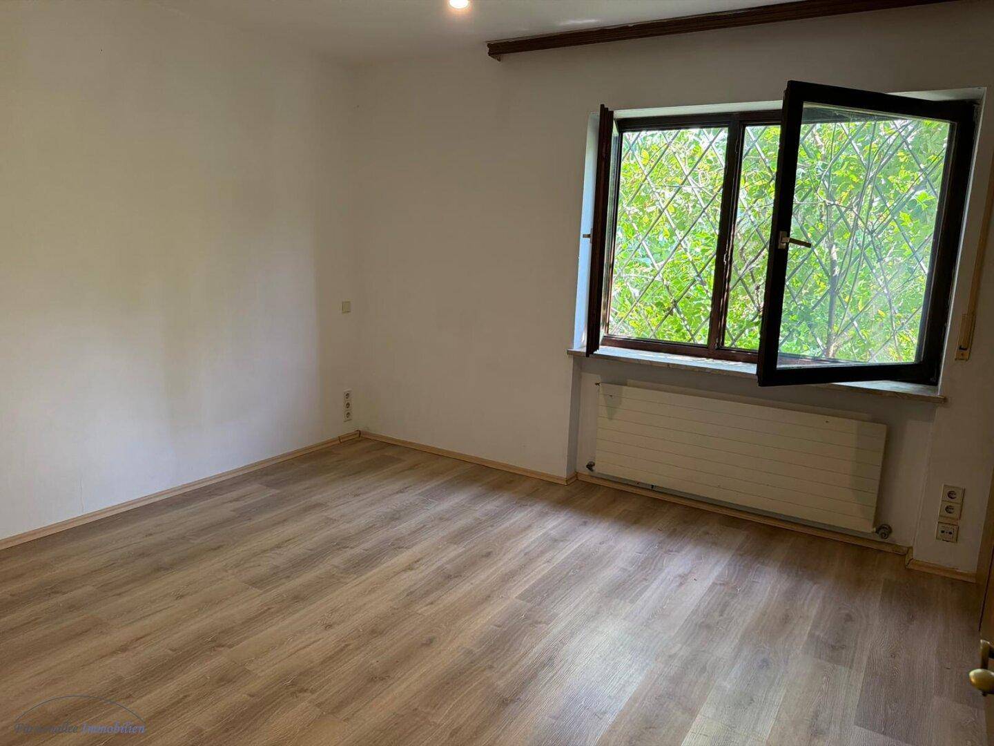 Schlafzimmer mit Laminatboden und Fenster zum Garten, bietet viel Tageslicht.