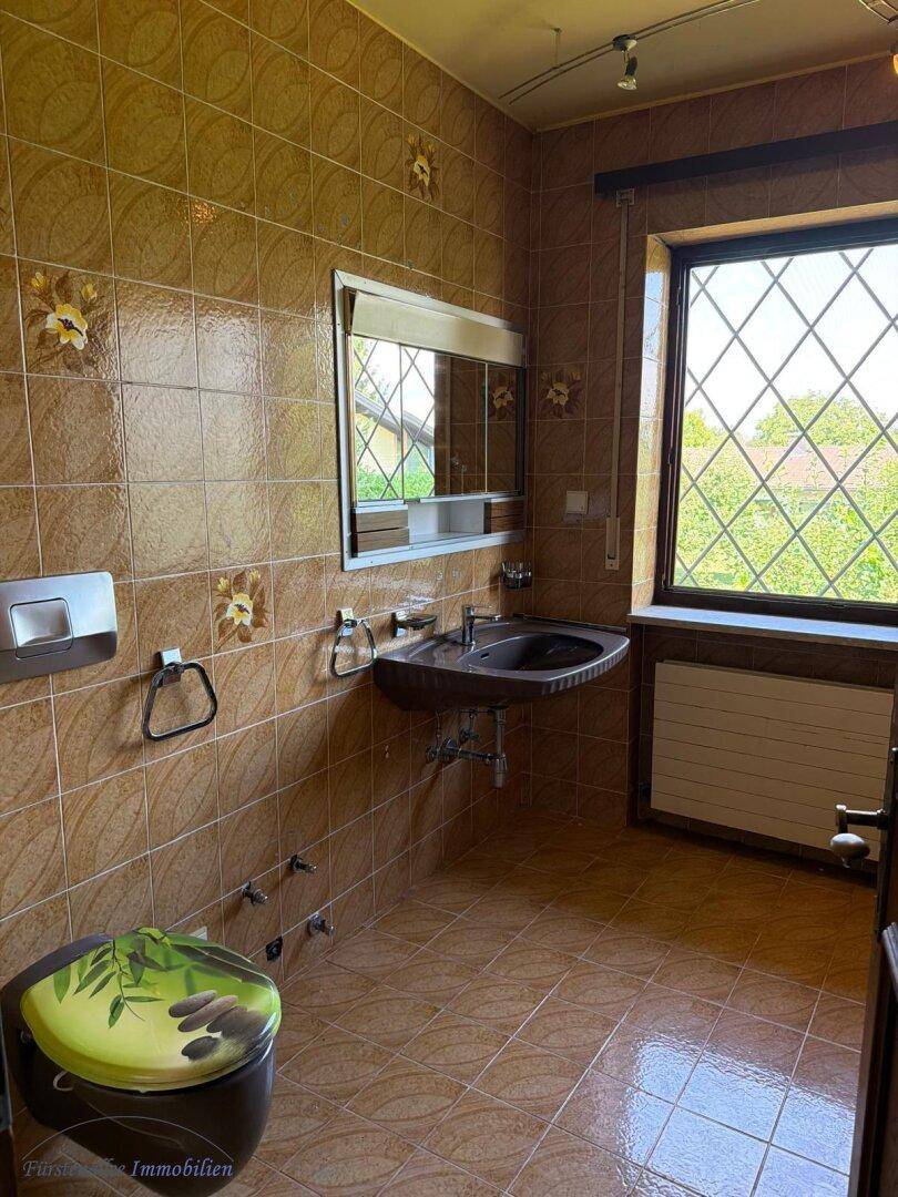Badezimmer mit braunen Fliesen, Waschbecken und Fenster mit Blick ins Grüne.