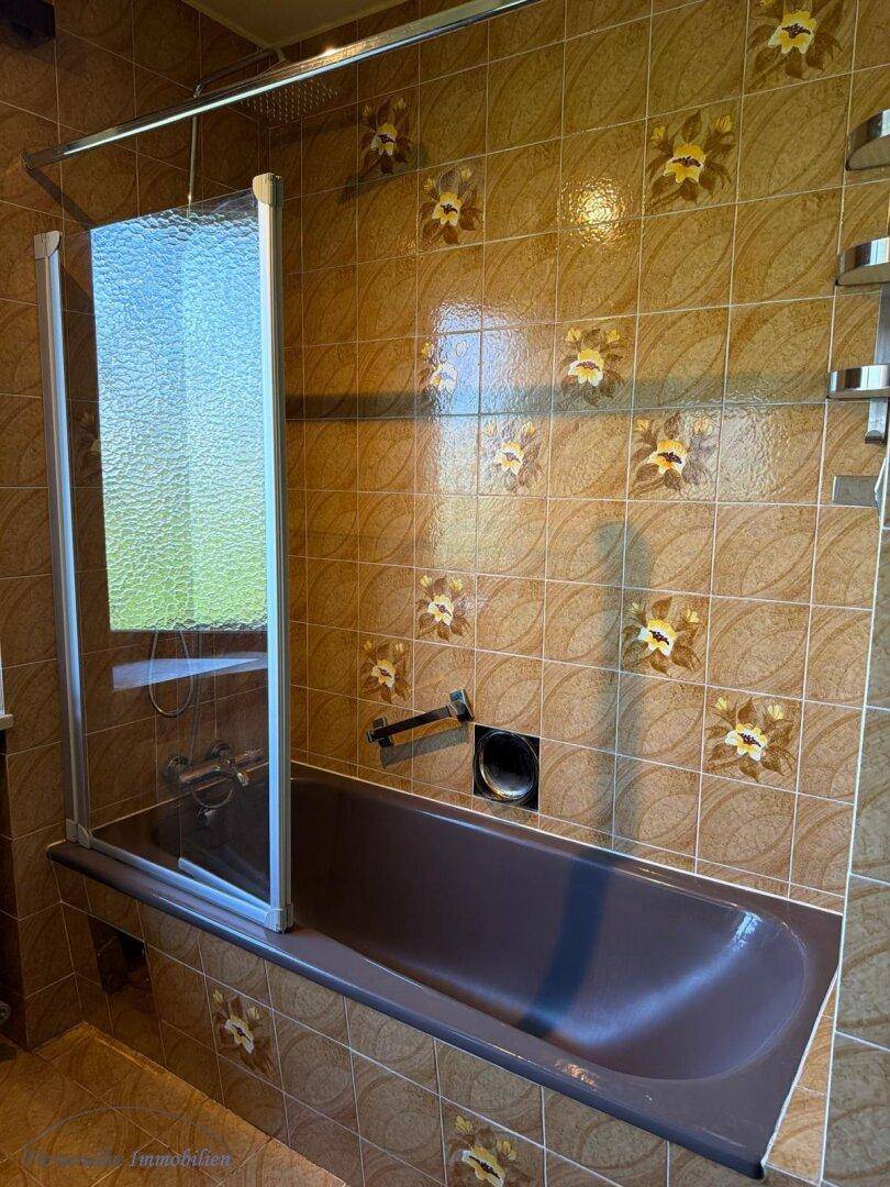 Badezimmer mit Badewanne, Duschabtrennung und braunen Wandfliesen.
