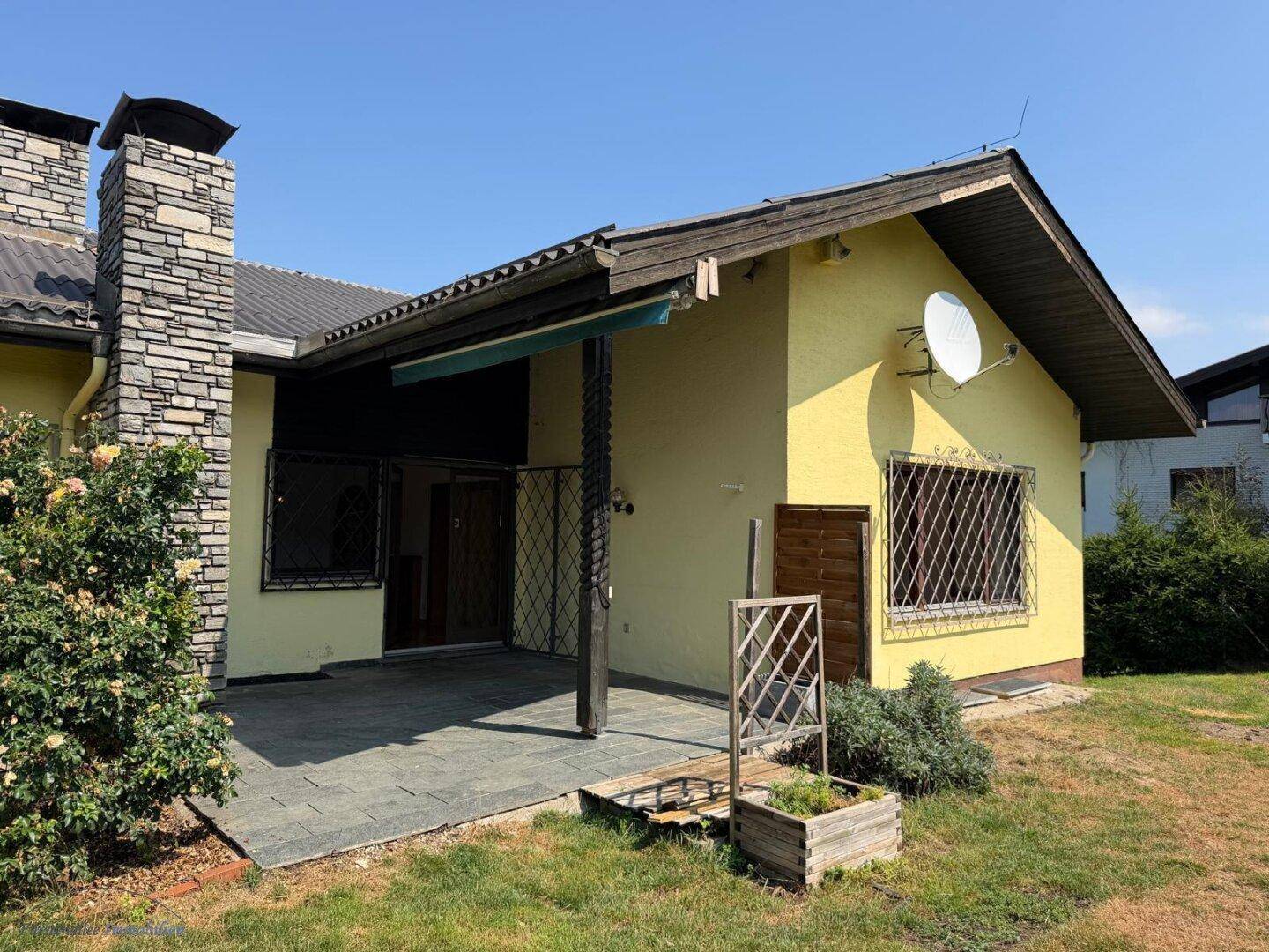 Rückseite des Hauses mit kleiner gepflasterter Terrasse und Steinkamin.