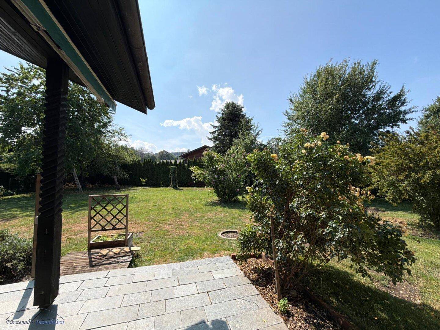 Blick von der Terrasse in den weitläufigen grünen Garten mit Bäumen und Sträuchern.
