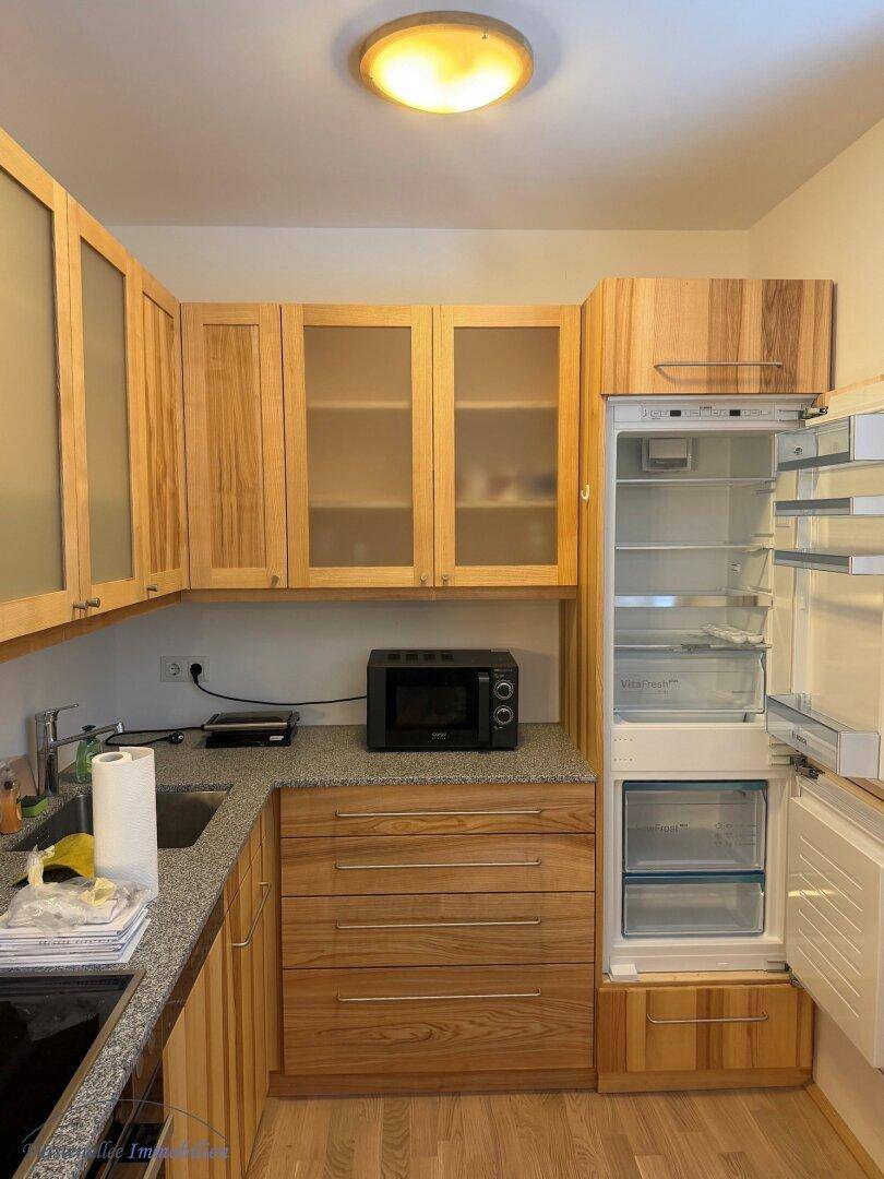 Funktionale Küche mit hellen Holzschränken, integriertem Kühlschrank und Mikrowelle.