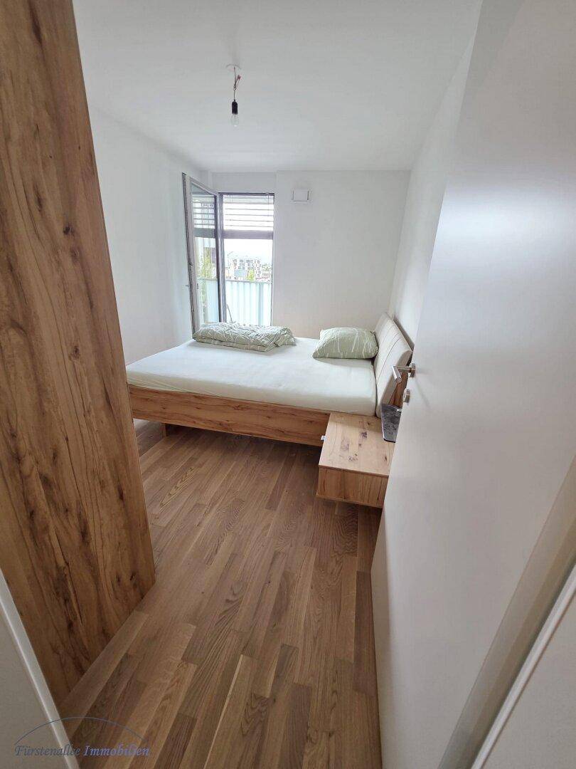 Helles Schlafzimmer mit Holzbett, Nachttisch und Zugang zu einem französischen Balkon.
