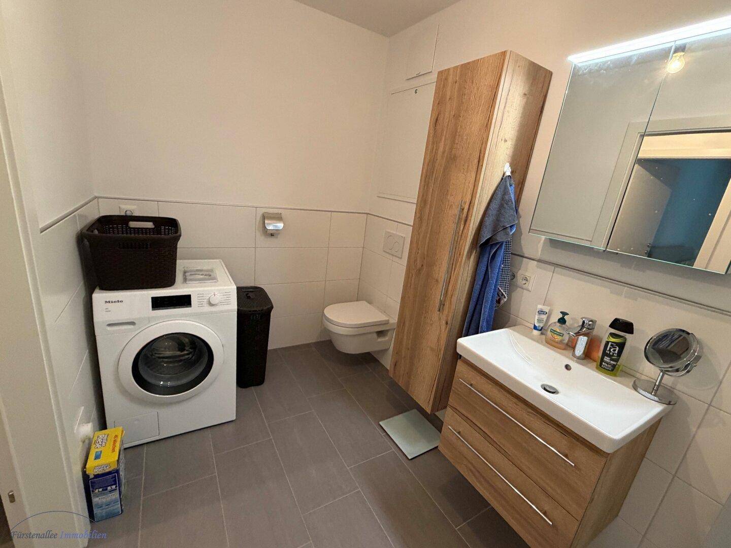 Badezimmer mit WC, Waschbecken, Waschmaschine und praktischem Stauraum.