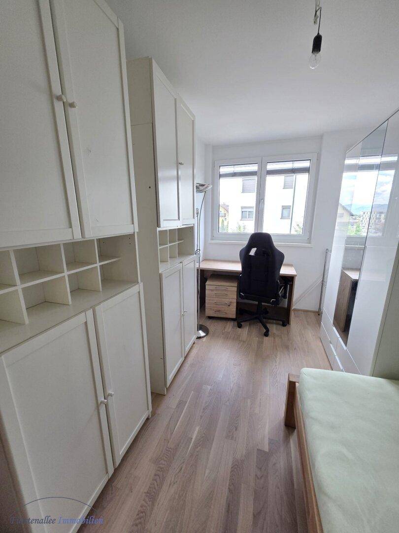 Helles Zimmer mit weißen Einbauschränken, Schreibtisch und Holzboden.