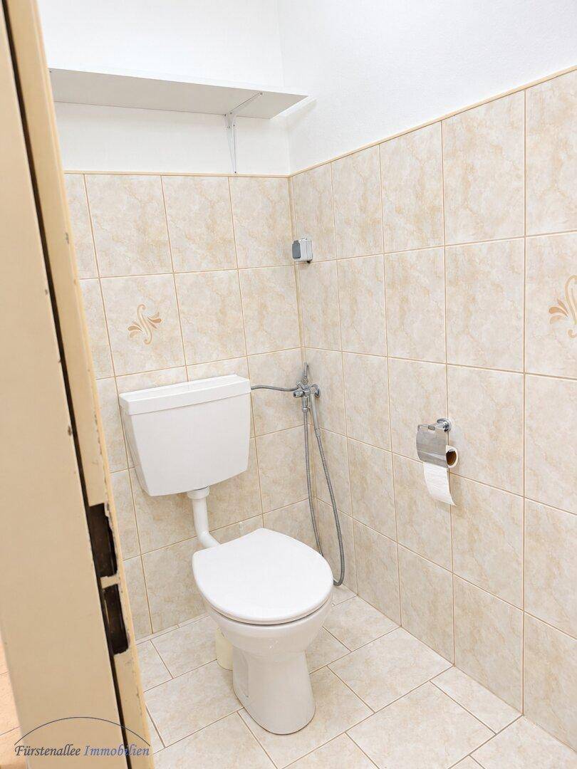 Separates WC mit beigefarbenen Fliesen und einfacher Toilette, ideal als Gästetoilette.