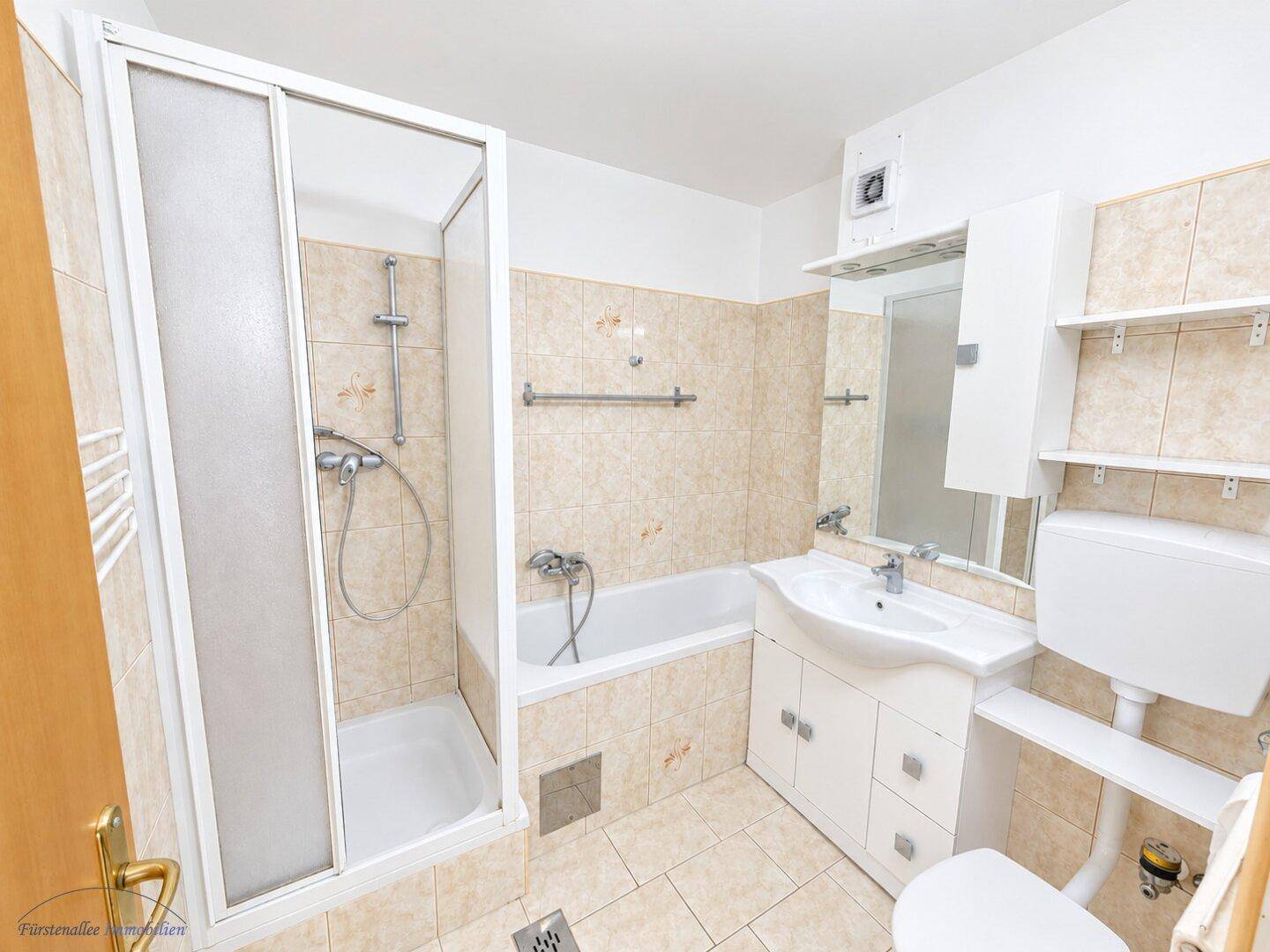 Gefliestes Badezimmer mit Badewanne, Duschkabine und Waschtisch mit Unterschrank in hellem Design.