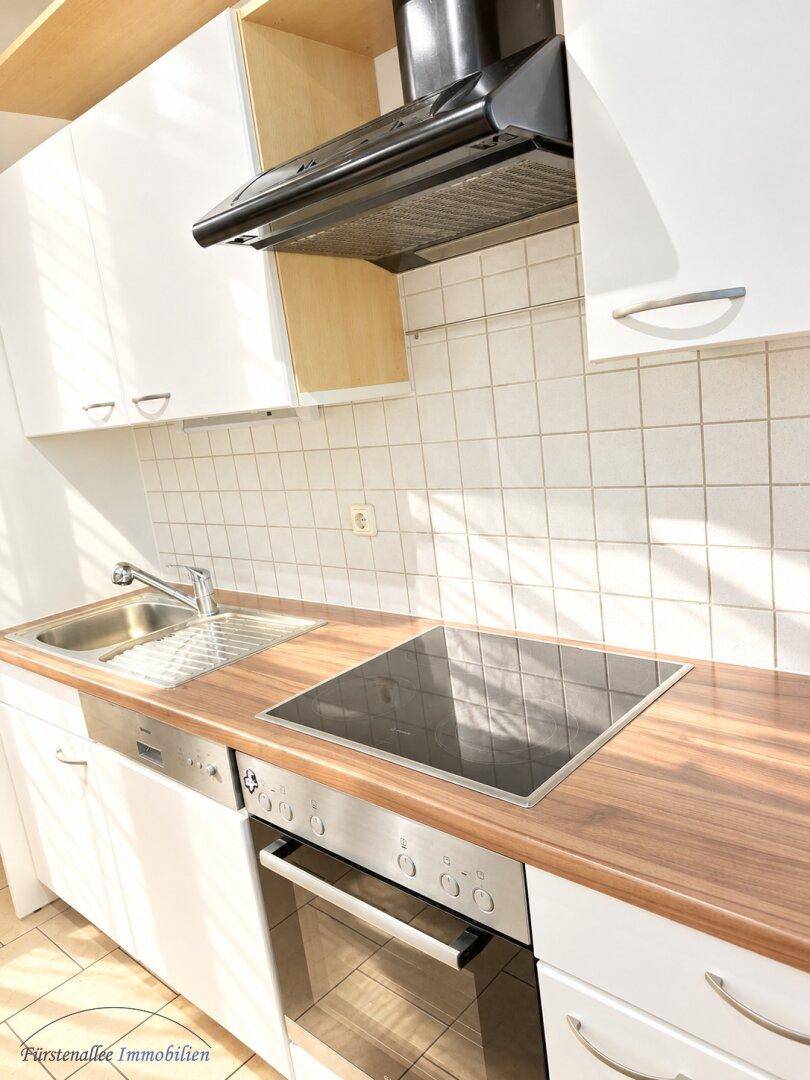 Detailansicht der Küchenzeile mit Induktionskochfeld, Backofen und Dunstabzugshaube für effizientes Kochen.