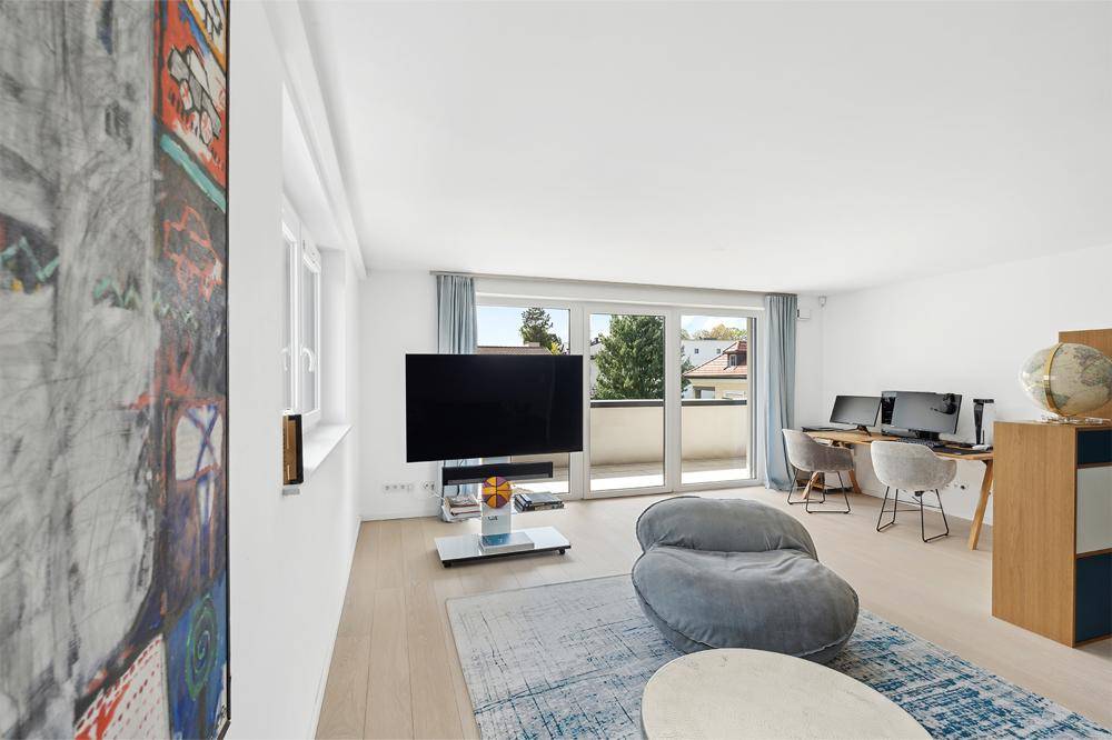 Helles Wohnzimmer mit Arbeitsbereich, hellem Holzboden und Zugang zum Balkon.