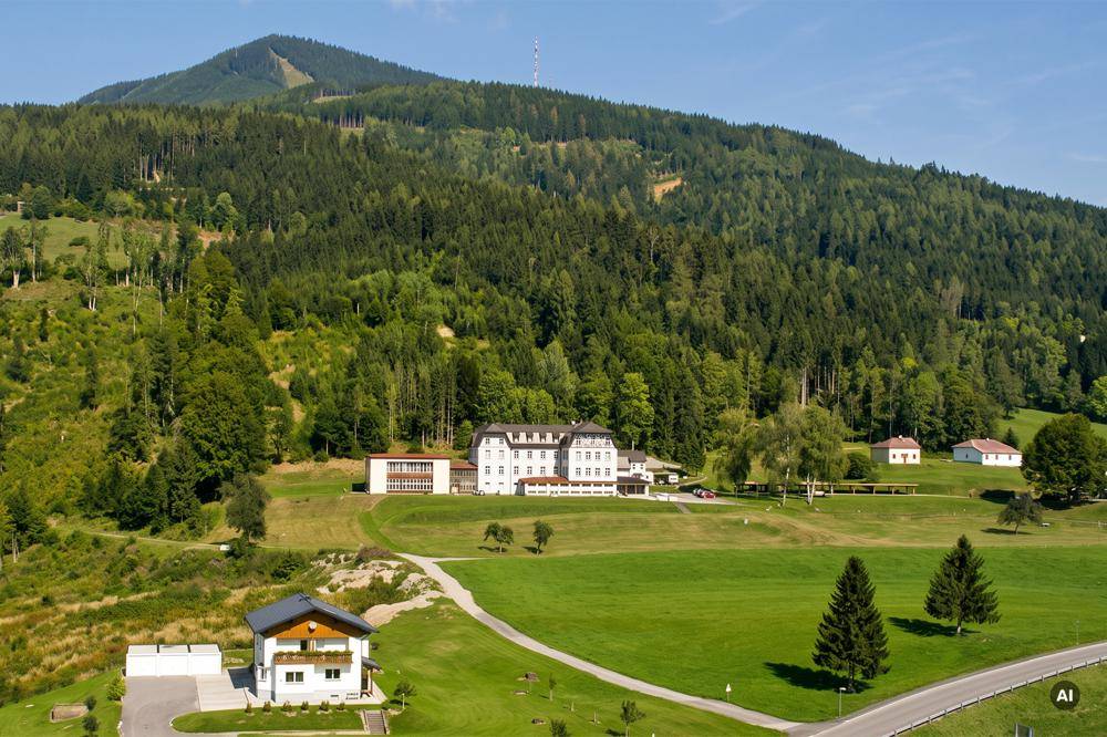 Panoramablick auf ein großes Anwesen mit einem Haupthaus und Nebengebäuden, eingebettet in eine grüne Berglandschaft.