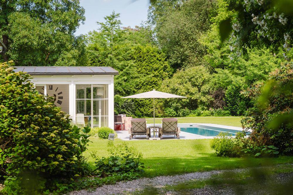 Idyllischer Gartenbereich mit Swimmingpool, Sonnenliegen und einem charmanten Wintergarten, umgeben von Bäumen.