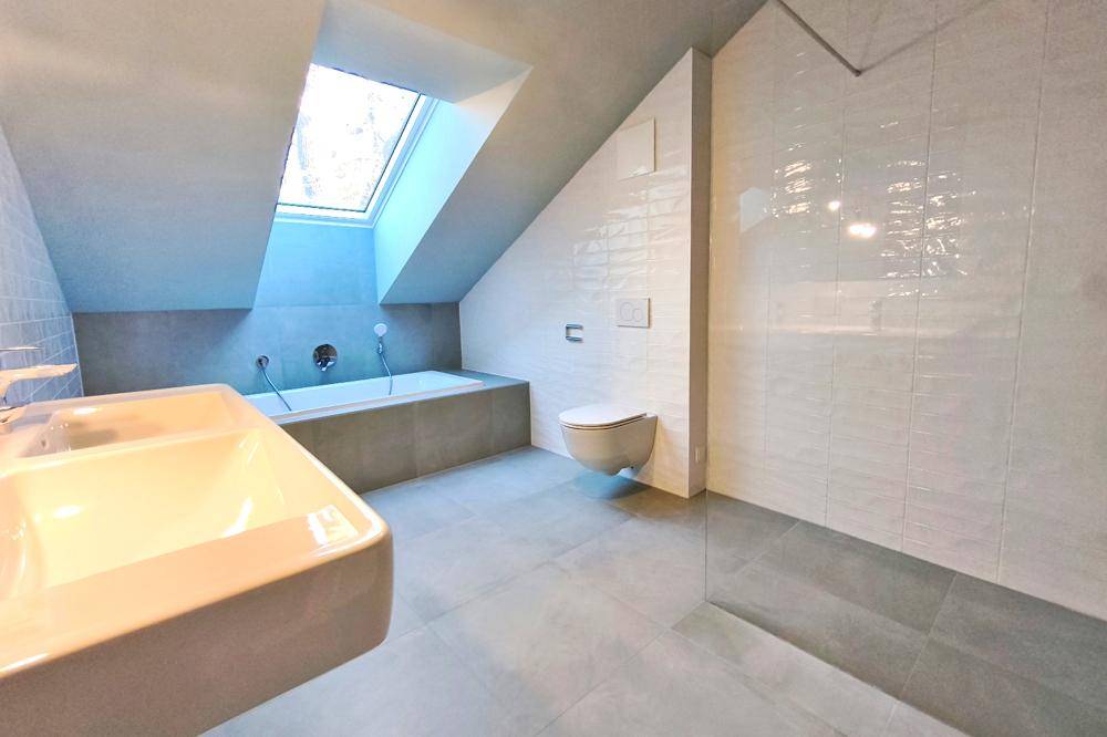 Modernes Badezimmer mit Badewanne unter einem Dachfenster, Wand-WC und stilvollen Fliesen.