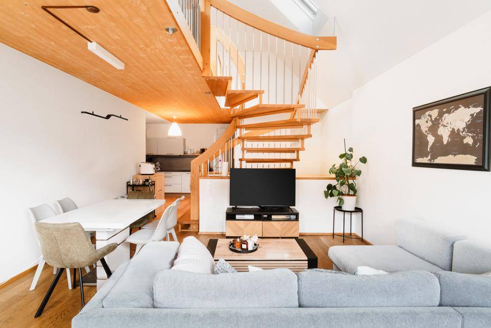Offener Wohn- und Essbereich mit moderner Einrichtung, Holzdecke und eleganter Wendeltreppe.