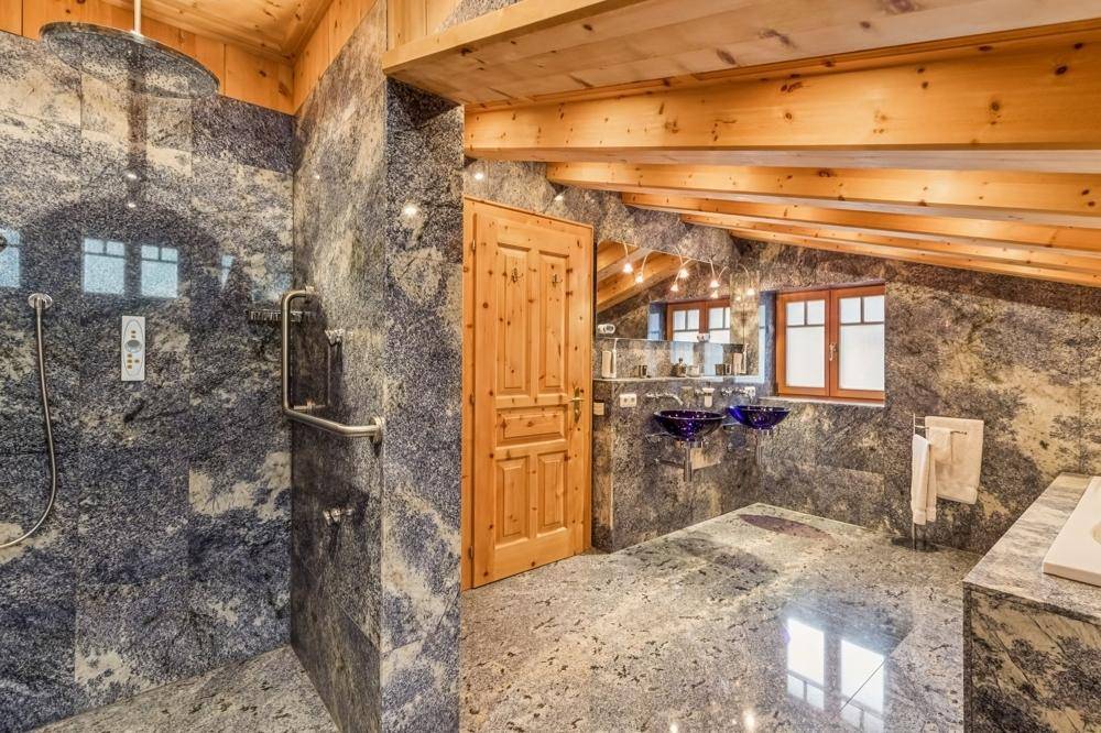 Luxuriöses Badezimmer im Dachgeschoss mit Granitfliesen, begehbarer Dusche und zwei Waschbecken.