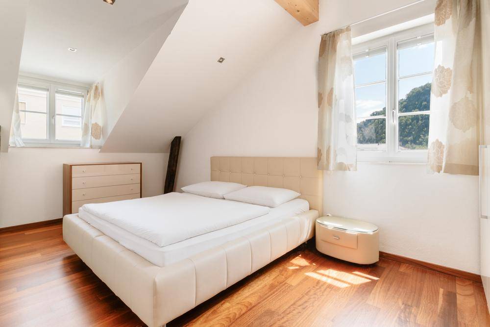 Helles Schlafzimmer mit Holzboden, Dachschrägen und großen Fenstern.