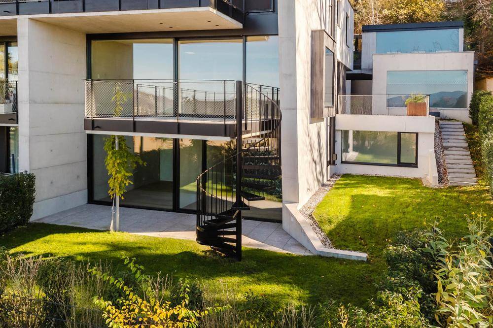 Moderne Architektur mit großen Glasfronten, Wendeltreppe und gepflegtem Gartenbereich.