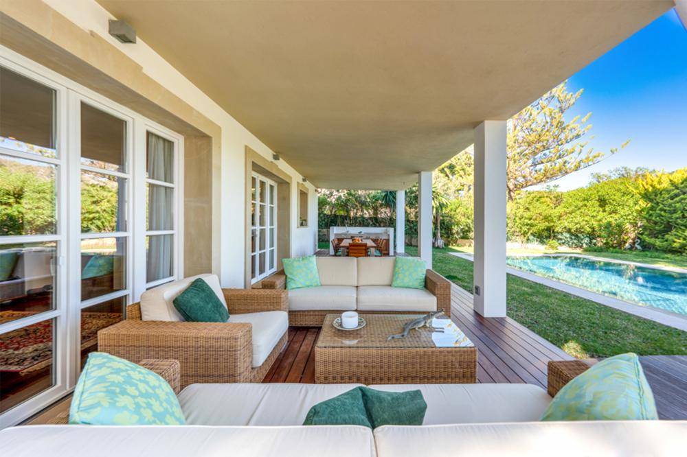 Gemütlicher Lounge-Bereich auf der überdachten Terrasse mit Blick auf den Pool und den Garten.