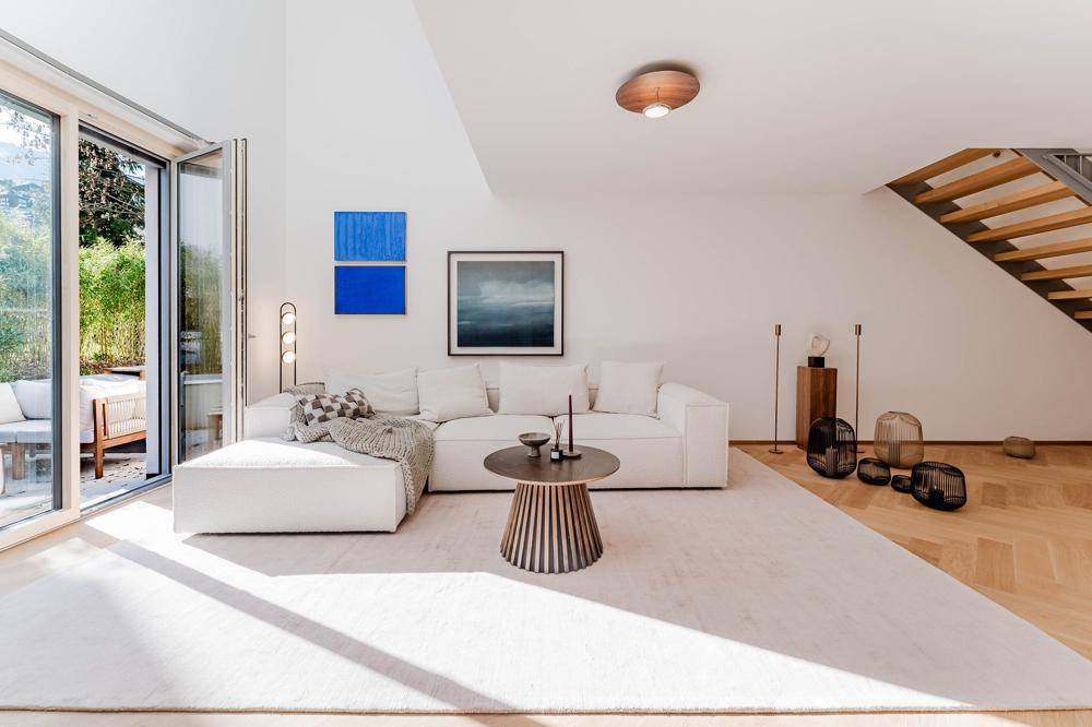 Lichtdurchflutetes Wohnzimmer mit großem Sofa, Parkettboden und Zugang zur Terrasse.