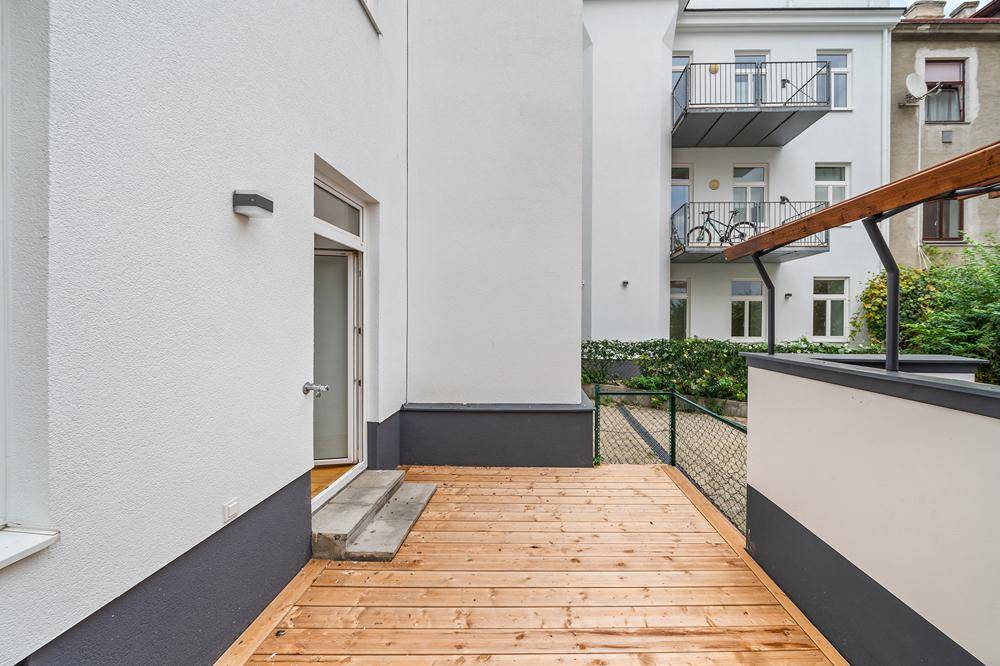 Geräumige Holzterrasse mit direktem Zugang zum Gebäude und Blick auf umliegende Balkone.
